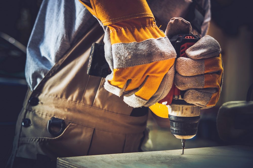 Construction worker wearing gloves drilling a piece of wood