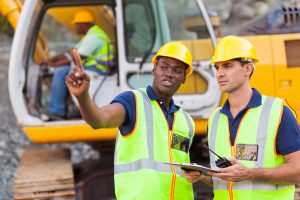 co-workers talking at construction site with bulldozer behind them