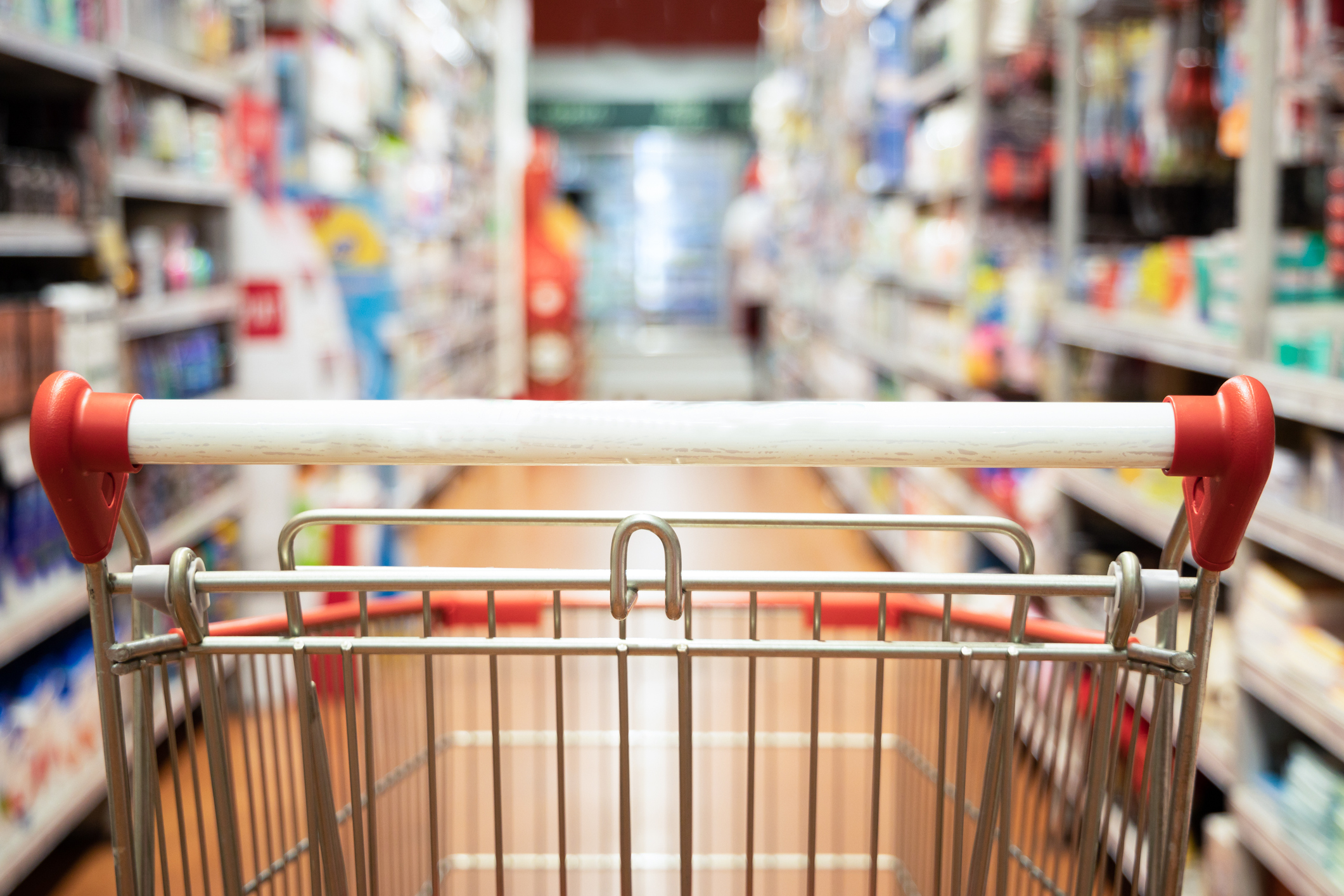 Perspective view of shopping trolley cart with modern supermarket aisle blurred background