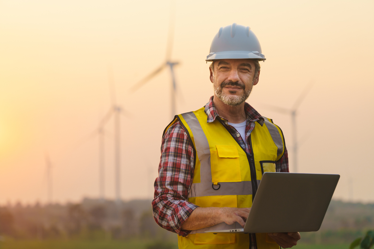 Man with a laptop standing in front of wind turbine