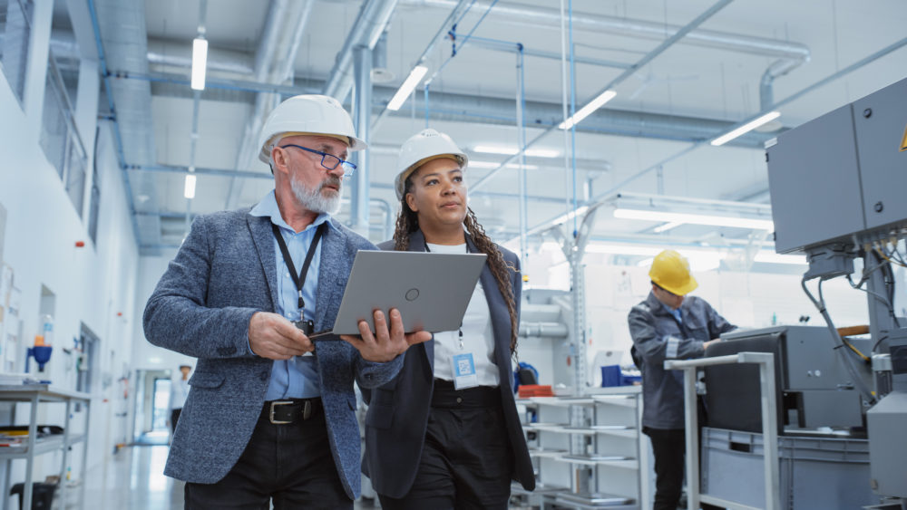 Managers walking through site with laptop, talking to employee