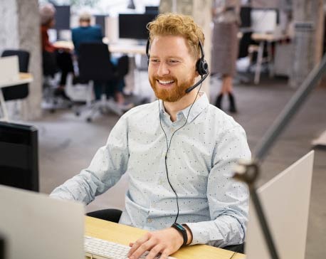 Smiling man is wearing headset as he works on a laptop